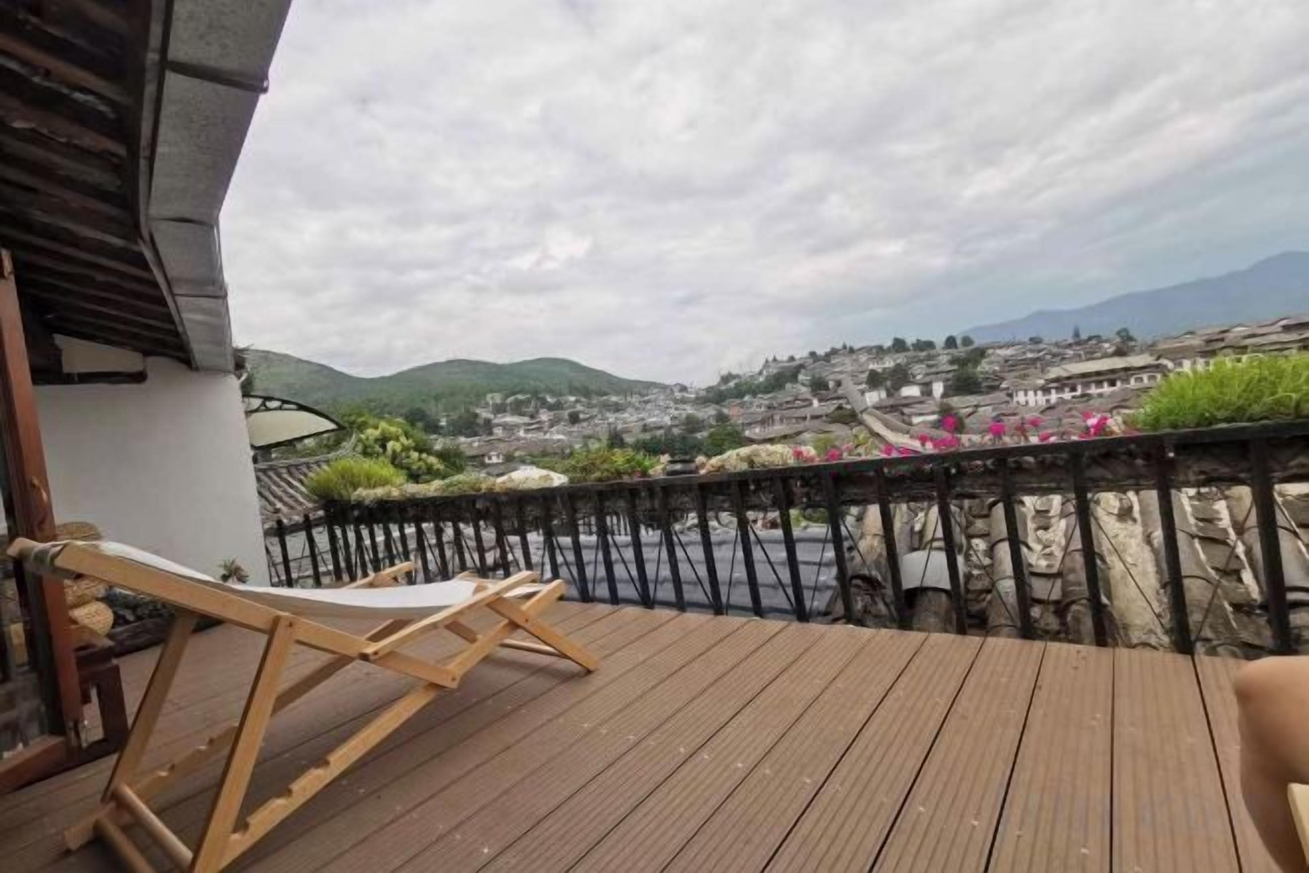 A wooden deck with a chair, overlooking a town with buildings and mountains.