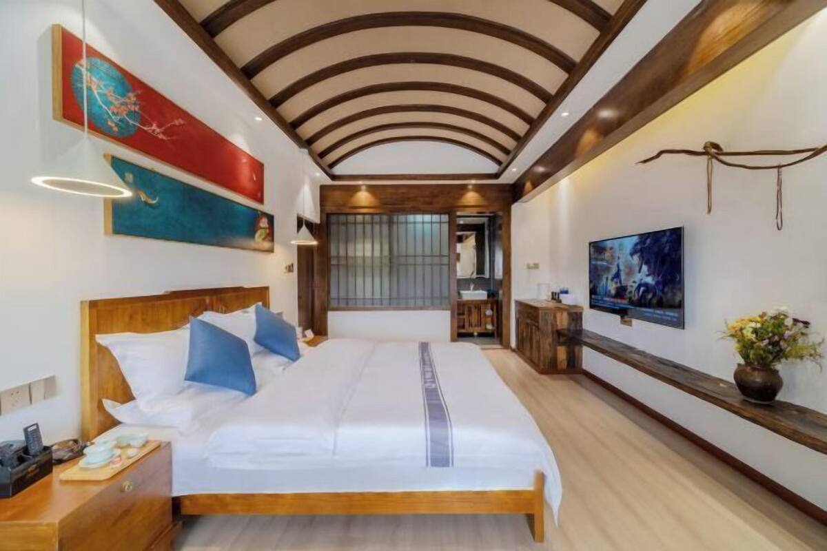 A hotel room with a large bed, wooden headboard, and a TV on the wall.