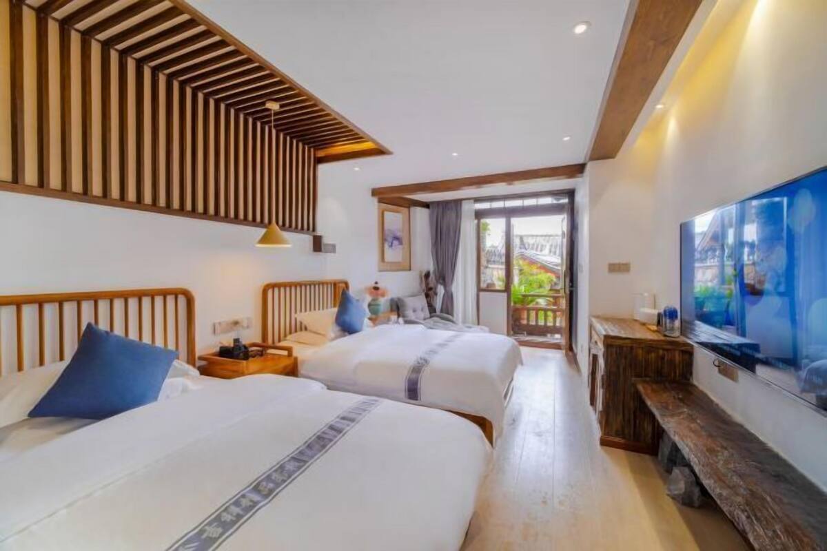 A hotel room with two beds, a wooden ceiling design, a TV, and a balcony with a view.