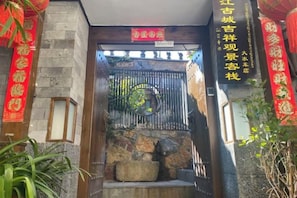 Une porte chinoise traditionnelle, avec des marches en pierre et un portail en métal, flanquée de banderoles rouges et d’une enseigne portant des caractères chinois.