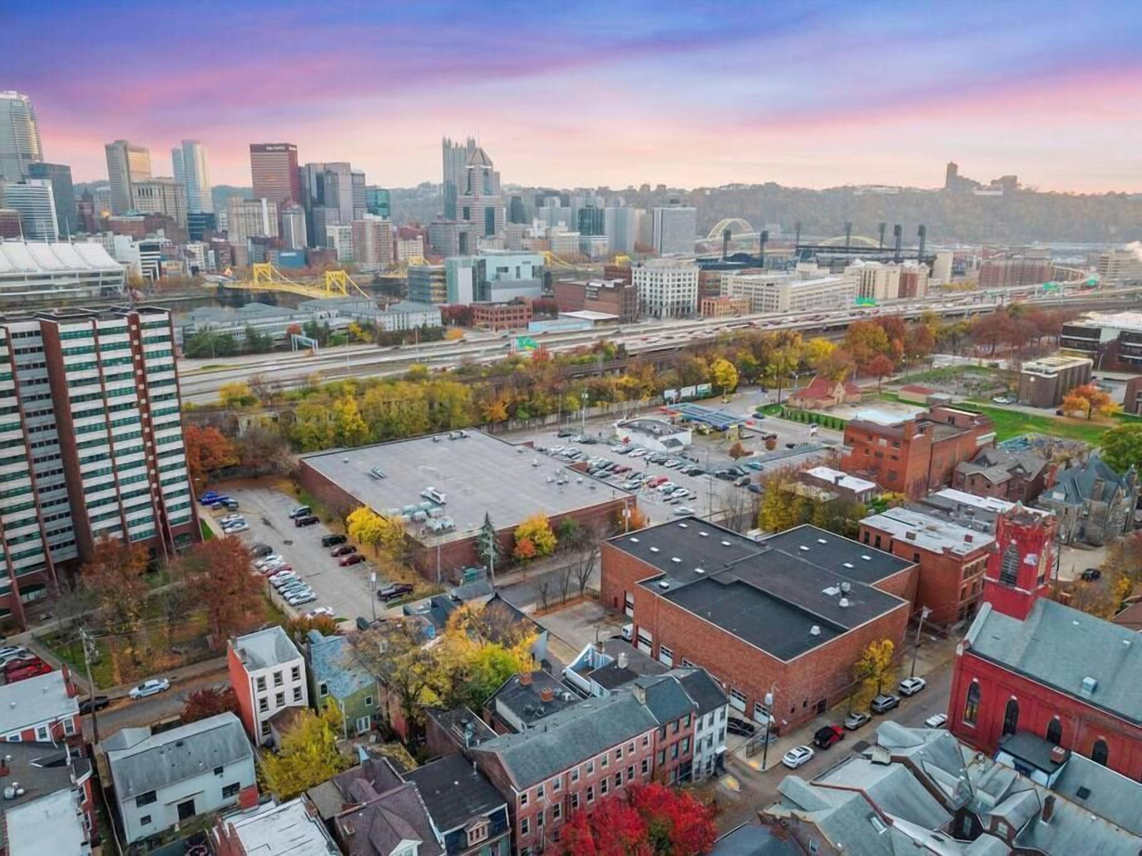 A cityscape with a mix of modern and older buildings, a parking lot, and autumn foliage.