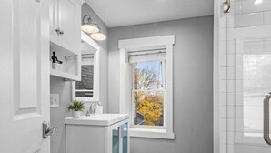Ein modernes Badezimmer mit einem weißen Waschtisch, einem Fenster mit Blick auf Herbstbäume und einer Duschkabine.