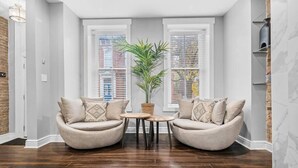 Ein modernes Wohnzimmer mit zwei beigen Sesseln, einem kleinen Holztisch und einem Blumentopf.
