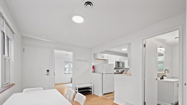 Una cocina moderna con armarios blancos, una isla central y una zona de comedor con mesa y sillas blancas.