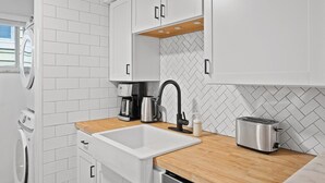 Una cocina moderna con armarios blancos, encimera de madera, un fregadero, una cafetera, un tostador y una lavadora.