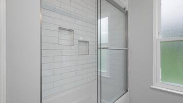 Ein modernes Badezimmer mit weißen Fliesen im U-Bahn-Stil, einer Duschkabine aus Glas und einem Fenster mit Milchglas.