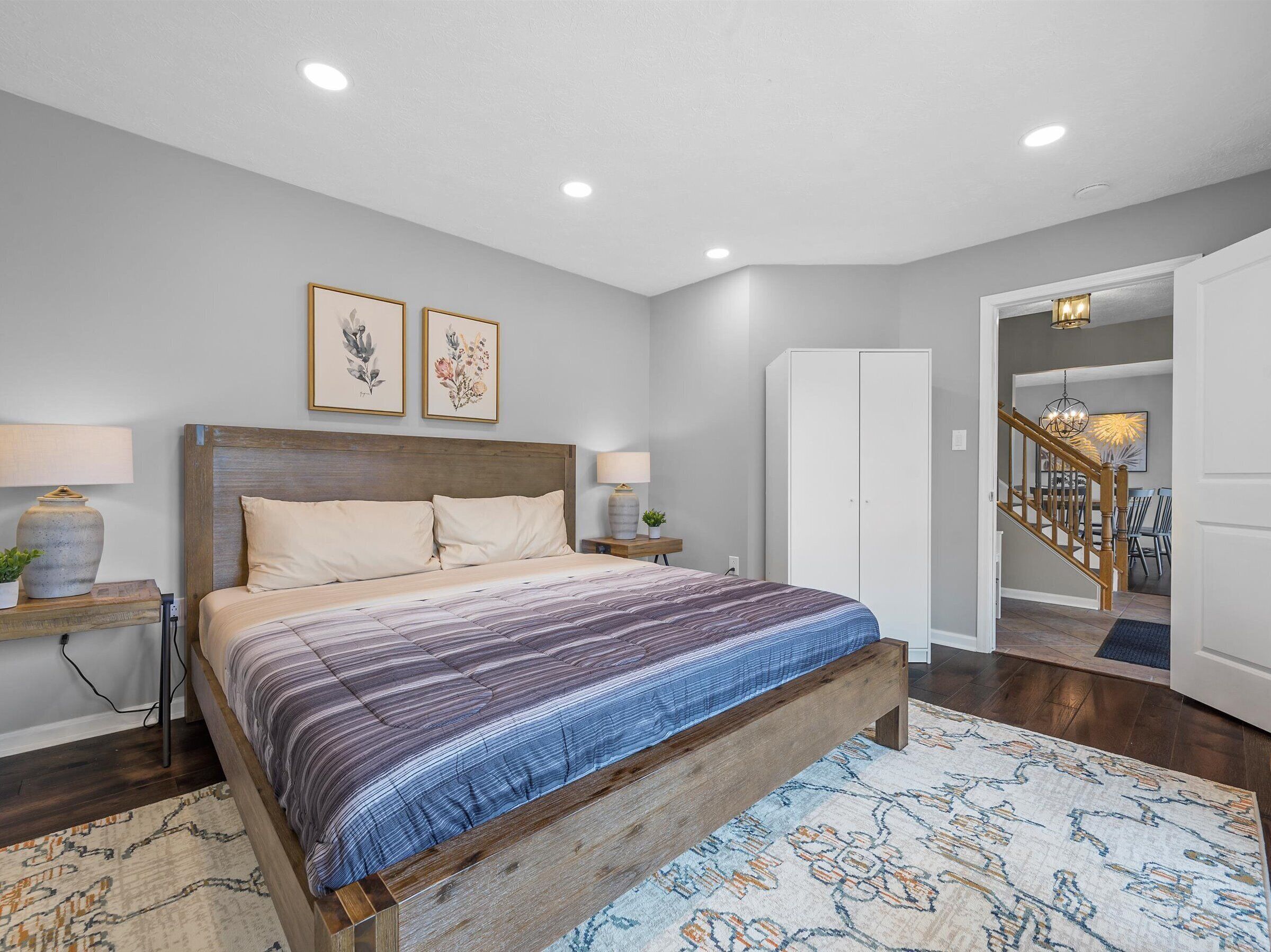 Une chambre à coucher avec un lit en bois, deux tables de chevet avec des lampes, une armoire et un escalier menant à une autre pièce.