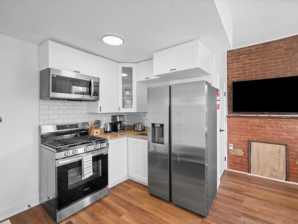 Una cocina compacta con electrodomésticos de acero inoxidable, armarios blancos y suelo de madera.