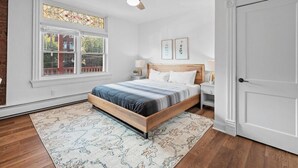 A bedroom with a wooden bed, a large window, a ceiling fan, and a door. - Shadyside, Pittsburgh, Modern and Accessible 2 Bedroom with Free Parking (Pittsburgh)
