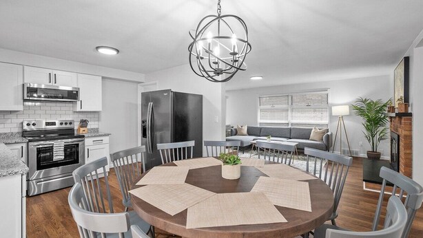 Una cocina moderna con electrodomésticos de acero inoxidable, un comedor con mesa y sillas redondas, y una sala de estar con sofá y chimenea.