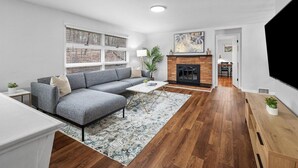 Una sala de estar moderna con un sofá seccional gris, una mesa de centro, una chimenea y un televisor.