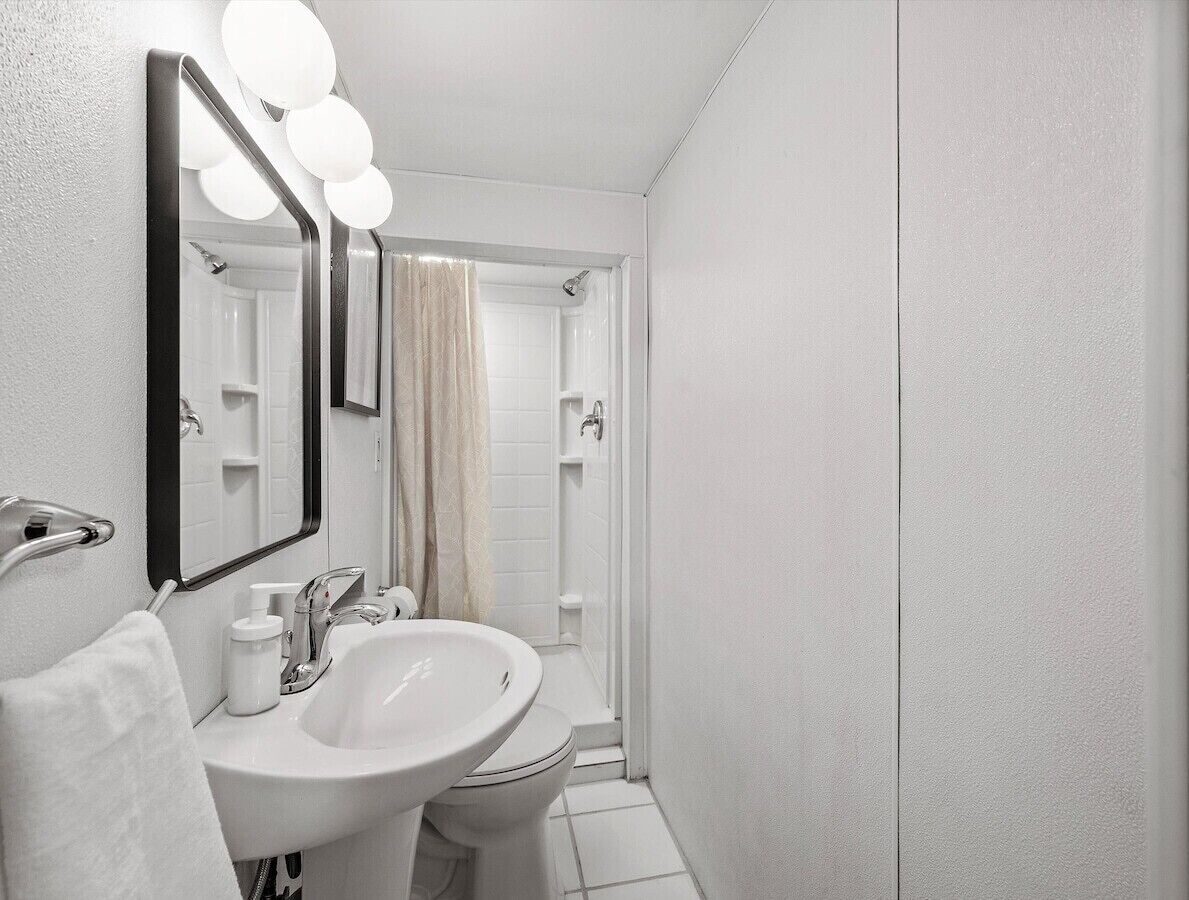 A bathroom with a white sink, a mirror with lights, a towel, and a shower area.