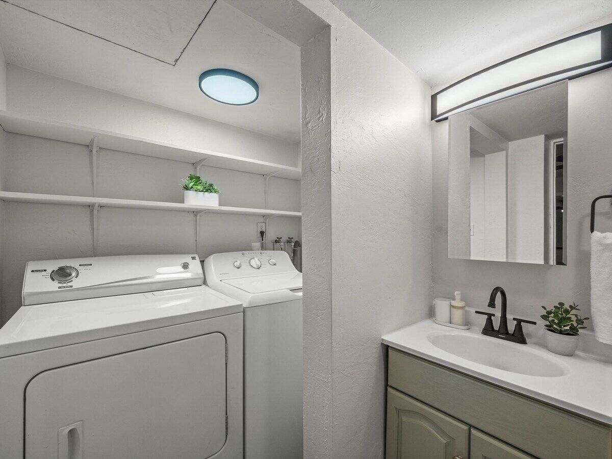 A compact, modern bathroom with a built-in washer and dryer, a sink, and a mirror.