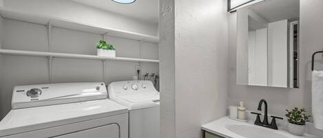 A compact, modern bathroom with a built-in washer and dryer, a sink, and a mirror.