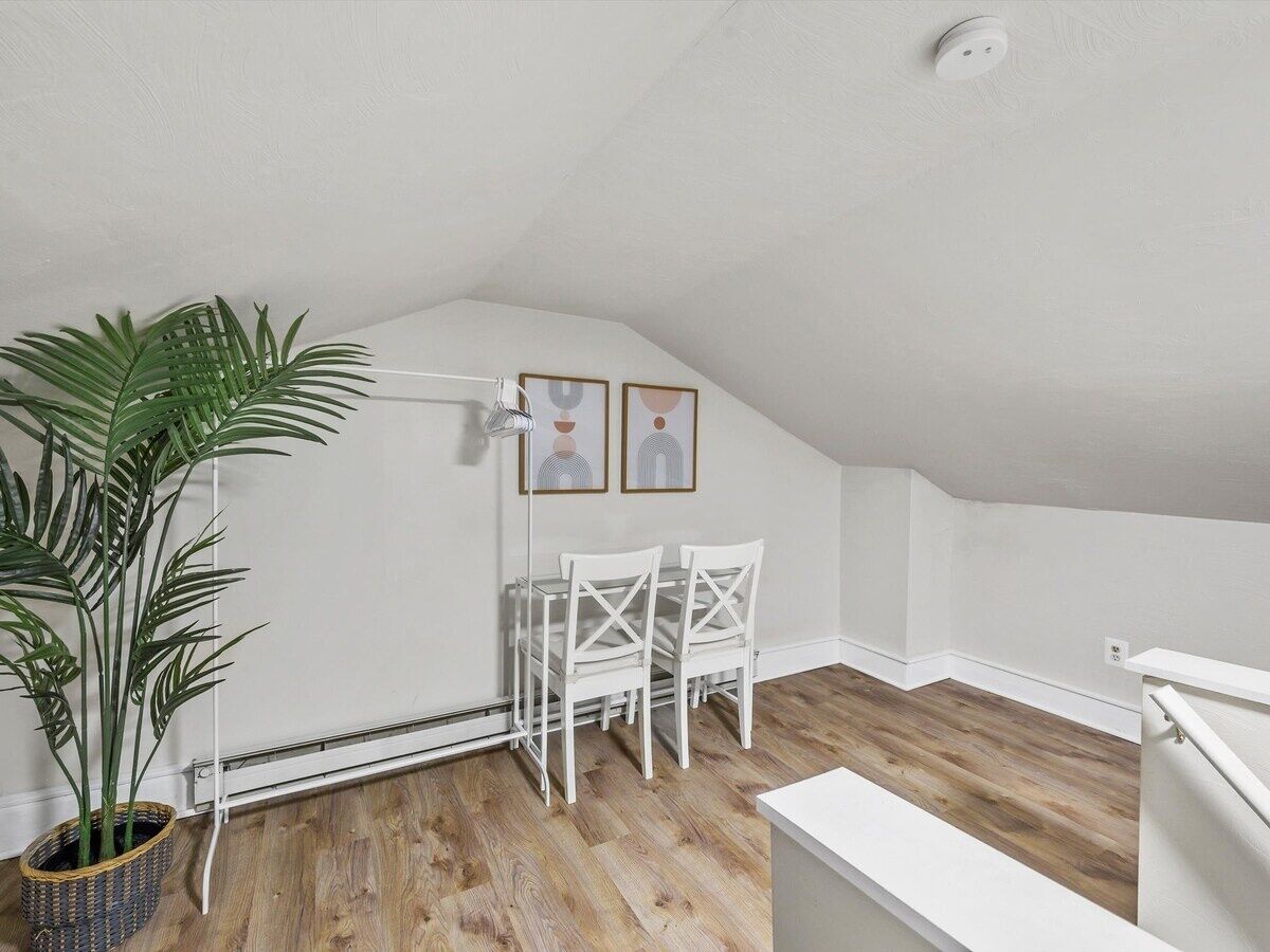 A room with a wooden floor, white walls, a ceiling fan, a potted plant, and a table with chairs.