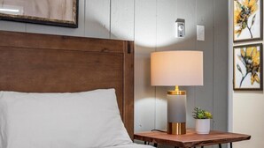 A neatly made bed with a wooden headboard, a bedside table with a lamp, and a small potted plant.