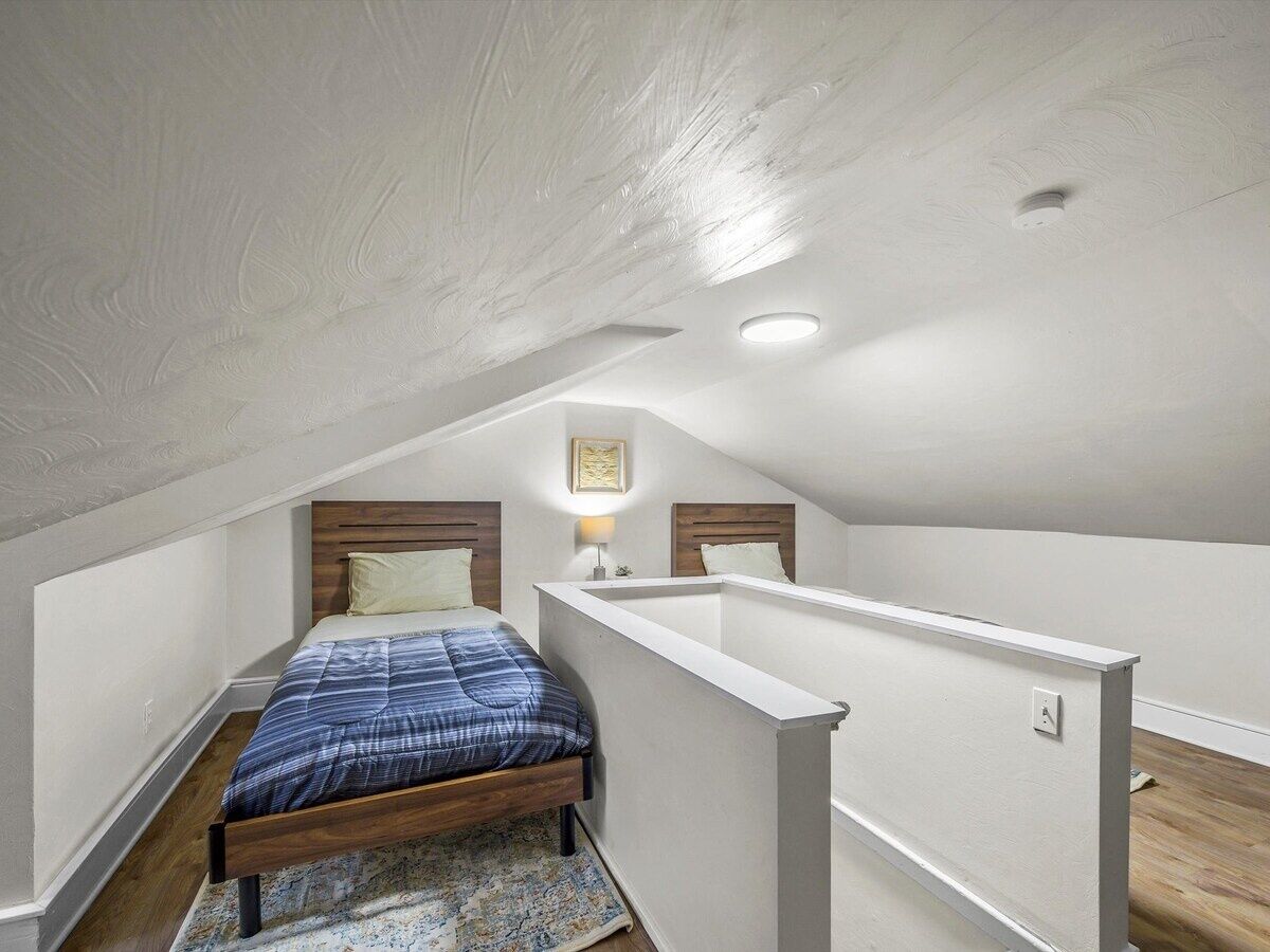 A bedroom with a sloped ceiling, a bed with a blue and white checkered bedspread, a nightstand with a lamp, and a small framed picture on the wall.