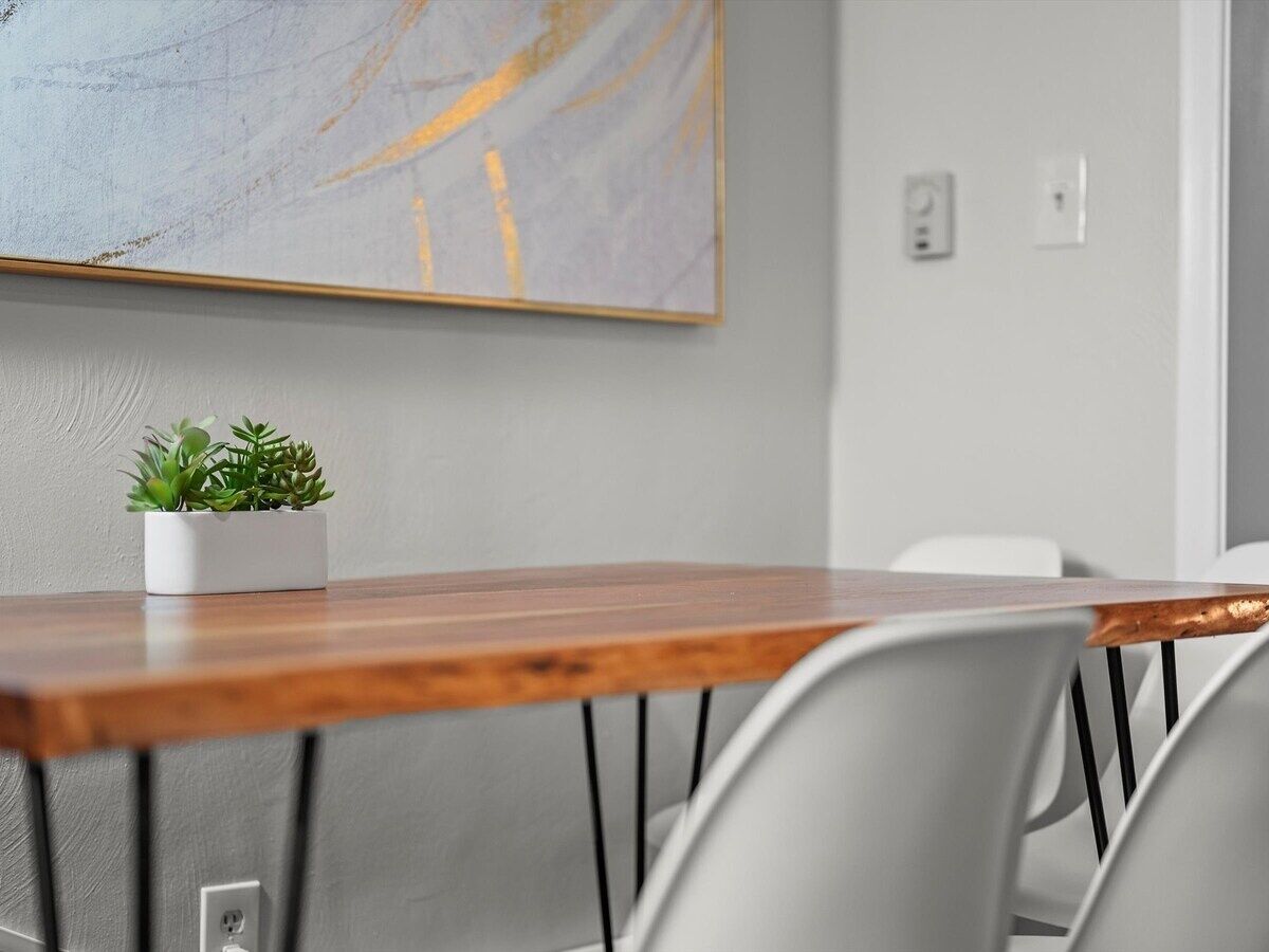 A conference room with a wooden table, white chairs, a potted plant, and a large abstract painting on the wall.