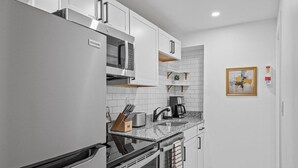 A compact kitchen with white cabinetry, a built-in oven, a microwave, and a coffee maker. - Shadyside, Central @4 Stylish and Central Studio with Free Parking (Pittsburgh)
