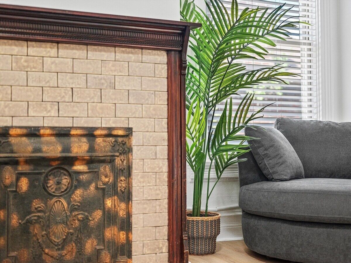 Ein Wohnzimmer mit Kamin aus Backsteinen, einem grauen Sofa und einem Blumentopf.