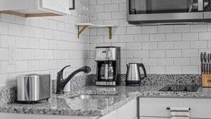 Une cuisine moderne avec des carreaux de céramique blancs disposés en motif métro, un grille-pain en acier inoxydable, une machine à café, une bouilloire et un bloc à couteaux.