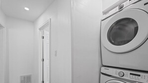 Une buanderie équipée de deux machines à laver Samsung superposées, d’une porte blanche et d’une bouche d’aération au mur.