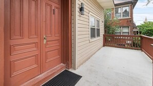 Ett garage som tillhör ett bostadshus, med en röd dörr, en liten veranda med ett träräcke och en klar himmel i bakgrunden.