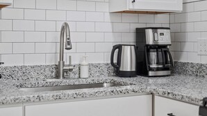 Una cocina con baldosas blancas tipo metro, un grifo de acero inoxidable, una cafetera y un hervidor sobre la encimera.