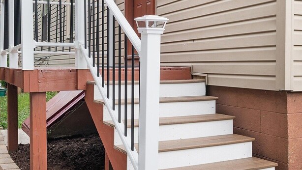 Fachada de una vivienda con terraza de madera, escalones blancos y puerta marrón.