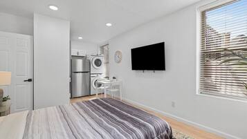 Ein Schlafzimmer mit Bett, Fernseher, Schreibtisch und einer Waschmaschine im Hintergrund.