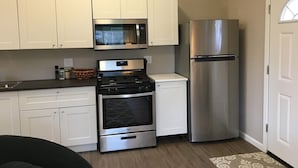 A compact kitchen with white cabinets, a stainless steel microwave, oven, and refrigerator. - Stagecoach Cottage quiet efficiency (Middletown)