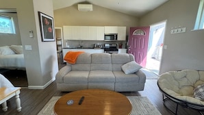 A living room with a sofa, a coffee table, and a chair. There is a kitchen in the background with cabinets and appliances. - Stagecoach Cottage quiet efficiency (Middletown)