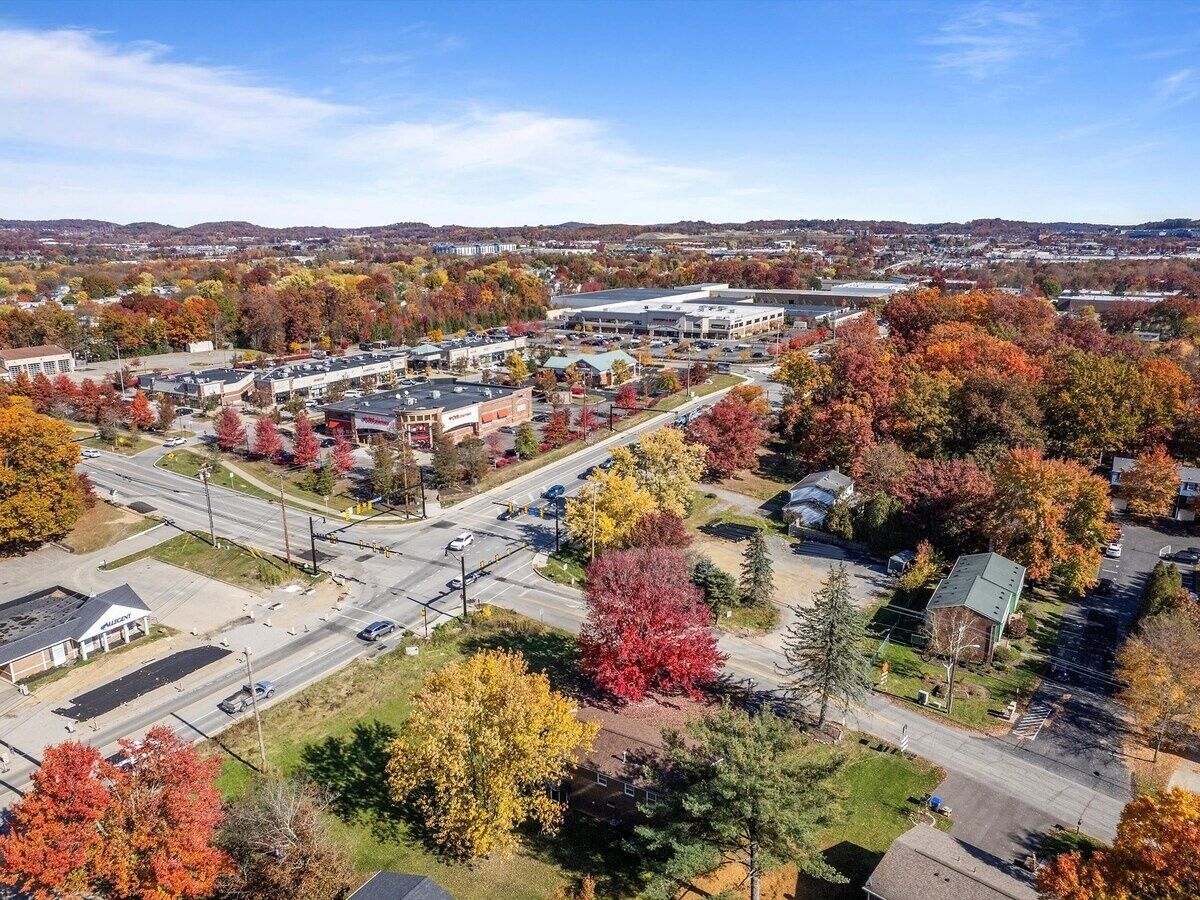 An aerial view of a town with a mix of commercial buildings, residential areas, and autumn-colored trees.
