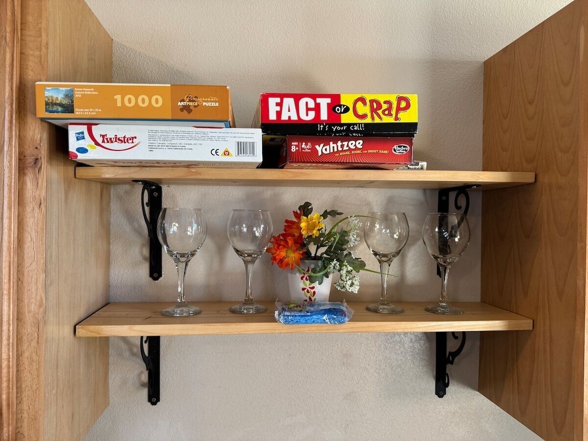 A shelf with four wine glasses, a vase with flowers, and three board games.