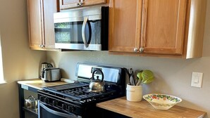 A compact kitchen with wooden cabinets, a stainless steel stove, a microwave, and a small countertop with a kettle and a bowl. - Emerald Lodge quiet efficiency (Middletown)