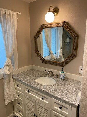 Een badkamer met een granieten aanrechtblad, een witte wasbak, een spiegel met een sierlijk omlijsting en een handdoek aan de muur.