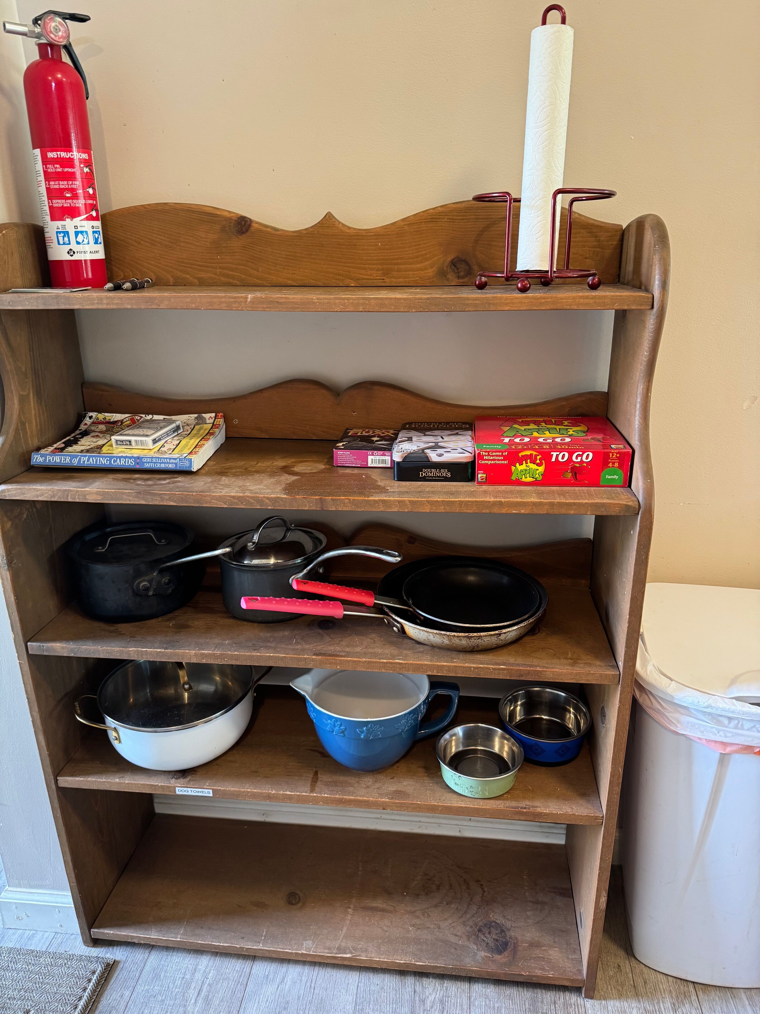 A wooden shelf with various kitchen items, including pots, pans, and a fire extinguisher.