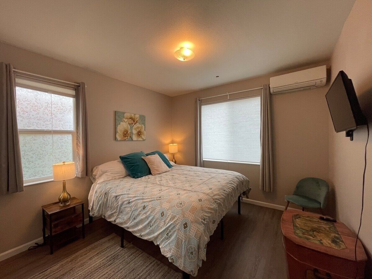 Een slaapkamer met een bed, twee nachtkastjes, een lamp, een stoel en een tv aan de muur.