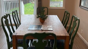 Un coin repas avec une table en bois, des chaises vertes, une plante en pot et un lustre.