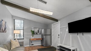 Un espacio habitable pequeño con kitchenette, sofá, televisor y banca.