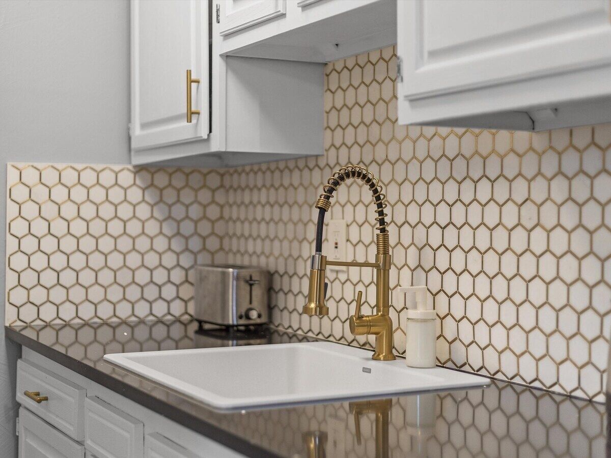 Una cocina con encimera blanca, grifo dorado y salpicadero con diseño de panal.