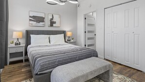 Een moderne slaapkamer met een groot bed, nachtkastjes met lampen, een bankje en een kledingkast.