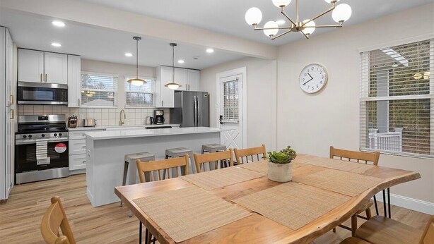 Una cocina moderna con armarios blancos, una isla central y una zona de comedor con mesa y sillas de madera.