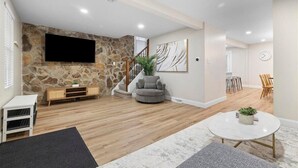 Una sala de estar moderna con una pared de piedra, un televisor de pantalla plana, un sillón gris y una mesa de centro redonda.