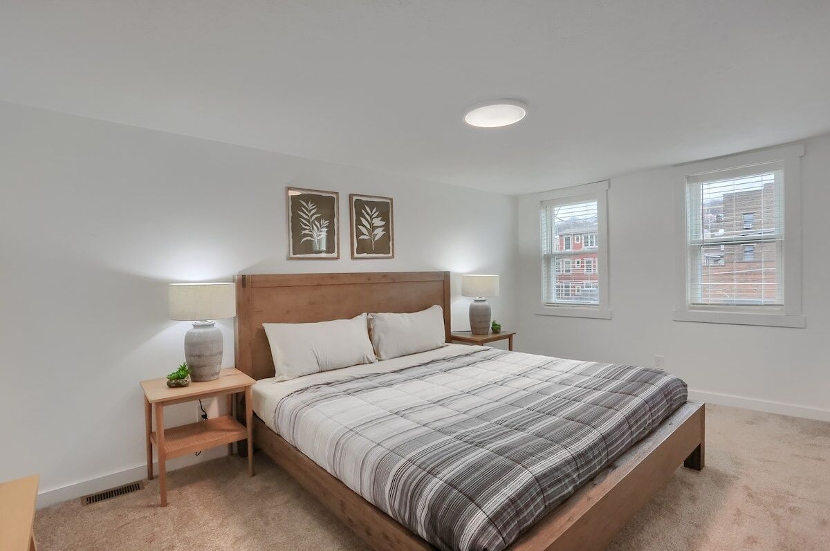 A bedroom with a bed, two bedside tables, a nightstand, a window, and two wall-mounted pictures.