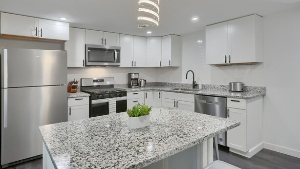 Cocina moderna con armarios blancos, encimeras de granito, electrodomésticos de acero inoxidable y una lámpara colgante espiral única.