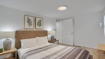 A bedroom with a bed, bedside tables, a nightstand, a lamp, a potted plant, and framed artwork on the wall.