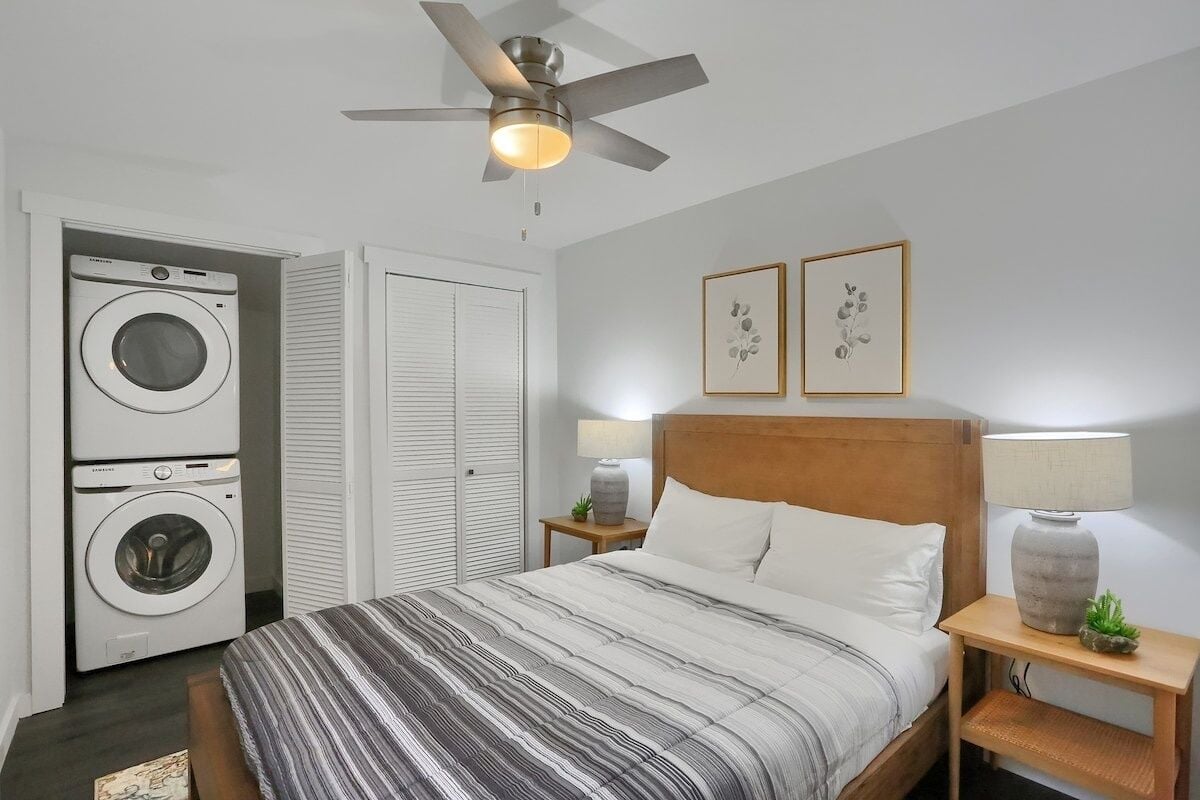 A bedroom with a bed, two wall-mounted lamps, a ceiling fan, and a washing machine in the corner.
