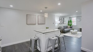 Una cocina moderna con una isla central, taburetes de bar y un área de comedor con sofá y mesa de centro.