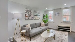 Una sala de estar moderna con un sofá gris, una mesa de centro blanca, una lámpara de pie y dos cuadros abstractos en la pared.
